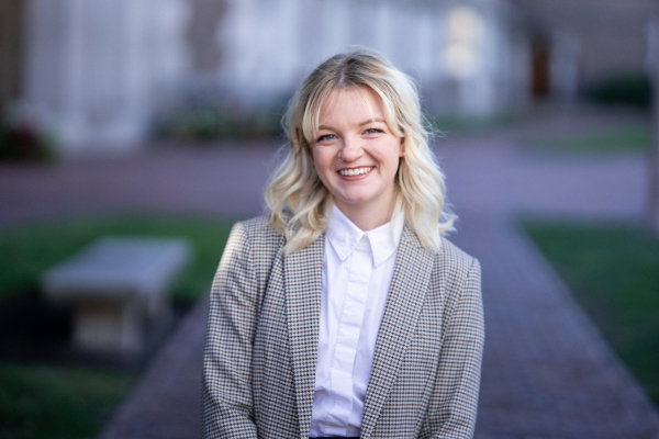 Willden smiling to the camera with her arms crossed behind in a campus background